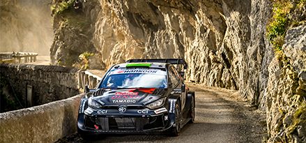Voiture de course Toyota roulant sur une piste en graviers surplombée par des rochers
