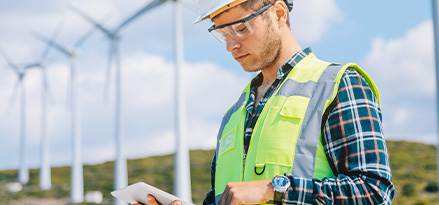 Un ingénieur se tenant devant des éoliennes et travaillant sur sa tablette