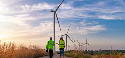 Un homme et plusieurs femmes marchant vers des éoliennes au coucher du soleil