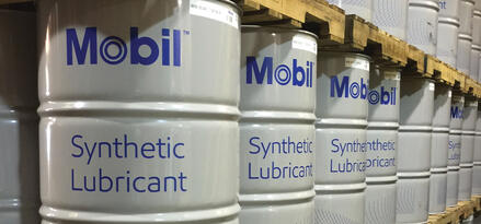 Fûts Mobil™ Synthetic Lubricant empilés sur palettes dans une allée d’entrepôt ordonnée.