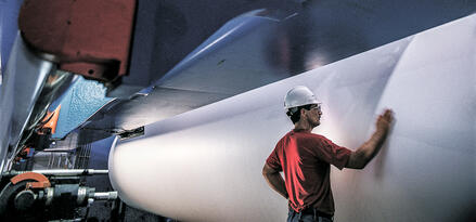 Ouvrier d'usine portant un casque inspecte une grande bobine de papier à l'intérieur d'une presse industrielle